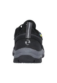 Chaussure de sport noire avec un dessus en mesh texturé, semelle en caoutchouc grise et une languette. Présente un logo près du talon et des accentuations réfléchissantes.