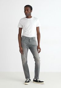 Jean en denim gris clair avec une coupe slim, un design à cinq poches et un léger délavage. Associé à un t-shirt blanc uni à col rond et des baskets noires.