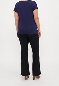 En kvinna som bär en marinblå kortärmad topp, svarta vida byxor med sidoklyftor och klackskor med leopardmönster, står med ryggen vänd mot kameran.