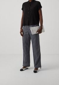 Black short-sleeve shirt with button closure, gray textured wide-leg pants, and a quilted white clutch. Footwear features black and silver accents.