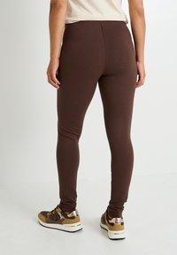 Leggings marrones hechos de material elástico, con un diseño ceñido y una textura suave, combinados con zapatillas de varios colores.