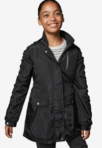 Giacca nera in nylon con colletto alto, tasca sul petto con zip, due tasche frontali e dettagli arricciati sulle maniche. Maglietta a righe sotto.