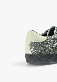 Sneaker featuring a glittery silver upper, light green suede heel tab, and a textured black rubber sole. Subtle brand lettering on heel.