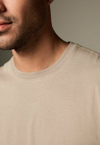 Beige bomulds T-shirt med rund halsudskæring og korte ærmer, med en glat tekstur og diskrete syninger.