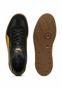 Fekete és sárga sportcipők, texturált velúrból és bőrből készült felső résszel, gumitalppal, amely hullámos mintázatú, és párnázott cipőnyakkal a kényelem érdekében.