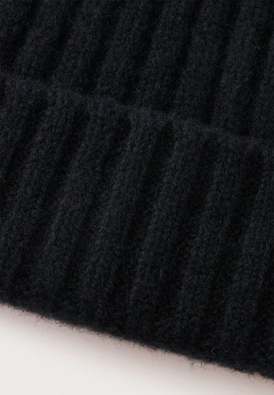 Gros plan sur un tissu tricoté côtelé noir avec une texture duveteuse, montrant des motifs tricotés verticaux et des fibres douces.