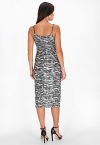 Schwarz-weiß gemustertes Midi-Kleid mit dünnen Trägern, texturiertem Stoff und einem Reißverschluss auf der Rückseite. Getragen mit schwarzen Stilettos.