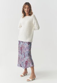 Hvid, tekstureret strikket sweater med en bred udskæring, parret med en blå silkesæt med paisleymønster og pink og lilla accenter. Hvide sandaler.