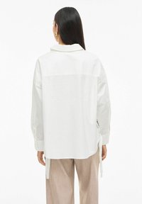 White, lightweight shirt with a back yoke, long sleeves, and adjustable side ties. Features a classic collar and smooth texture.
