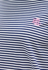 Ύφασμα με οριζόντιες ρίγες σε μπλε και άσπρο, με μικρά ροζ κεντημένα γράμματα «RLL» στην πάνω δεξιά πλευρά.