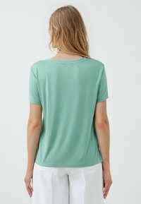 T-shirt verde menta a maniche corte realizzato in tessuto morbido con scollatura rotonda e taglio dritto, caratterizzato da dettagli di cucitura sottili.