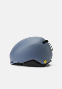 Čelada z gladko, mat modro zunanjostjo, zaobljeno obliko in sivo tkaninsko podlogo. Ima rumeno oznako MIPS in ventilacijski trak.