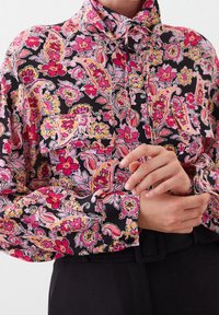 Long-sleeve shirt in black fabric adorned with a colorful floral paisley pattern in pink, yellow, and white, featuring button details and a collar.