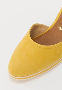 Chaussure slip-on en suède jaune avec un bout arrondi, présentant un intérieur lisse et une semelle intermédiaire blanche subtile avec des accents jaunes.