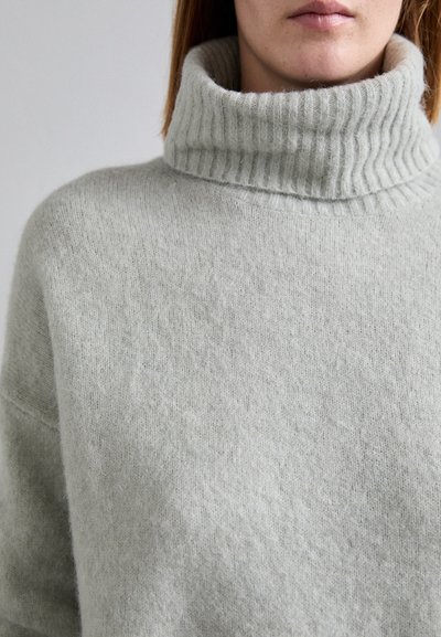 Maglione grigio chiaro in maglia con un ampio collo a dolcevita a coste. Il tessuto appare morbido e testurizzato, con una vestibilità comoda e dettagli minimi.