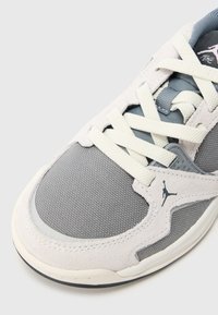 Ανοιχτό γκρι αθλητικό παπούτσι με υφασμάτινο επάνω μέρος με υφή, λείες σουέντ λεπτομέρειες και λευκά κορδόνια με ξεχωριστό λογότυπο στη πλευρά.