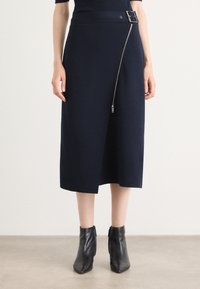 Jupe marine de longueur genou avec une large taille et un détail de fermeture éclair diagonal. Fabriquée en tissu doux, avec une accentuation de boucle de ceinture.