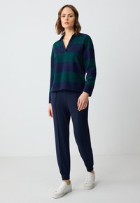 Gebreide pullover met donkergroene en marineblauwe strepen, met een kraag en een losse pasvorm. Gecombineerd met marineblauwe tapered broek en witte sneakers.