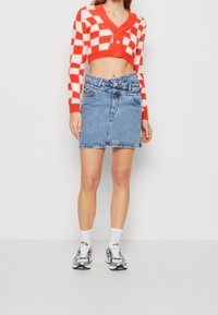 Röd och vit rutigt kort tröja med tre knappar och en ljusblå denim-minijurk, matchad med vita strumpor och silverfärgade sneakers.