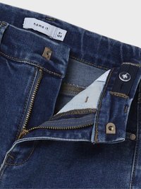 Mörkblå denimjeans med dragkedja, metalldetaljer och kontrasterande beige sömnad. Etikett inuti visar märke och storlek.