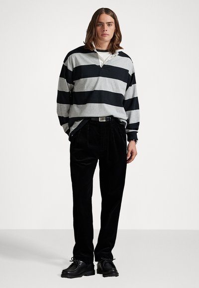Camisa de manga larga a rayas en gris y negro con cuello, combinada con pantalones de corcord gris oscuro y zapatos negros, de pie sobre un fondo simple.