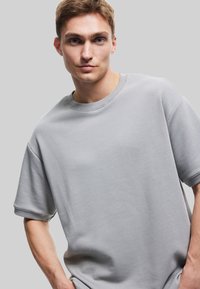 Lys grå kortærmet sweatshirt med rund hals og ribbede manchetter. Blød, ensfarvet tekstil med en afslappet pasform.