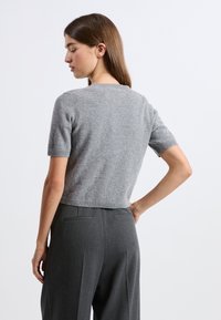 Szary krótki sweter z dzianiny z okrągłym dekoltem, o kroju cropped i miękkiej fakturze, zestawiony z dopasowanymi ciemnoszarymi spodniami.