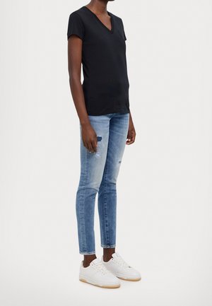 Musta V-pääntie t-paita, lyhyet hihat, yhdistettynä vaaleansinisiin kuluneisiin slim fit -farkkuihin ja valkoisiin tennareihin, joissa on kumipohjat.