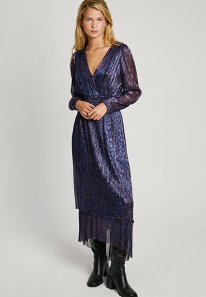 Robe violette plissée avec un décolleté en V profond et de longues manches transparentes. Présente un ourlet à volants et est portée avec des bottes noires jusqu'aux genoux.