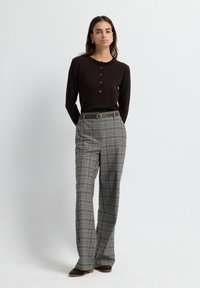 Lange mouwen bruin top met knoopdetails, gecombineerd met grijze geruite high-waisted broek en een bruine riem. Glad textuur, ontspannen pasvorm.