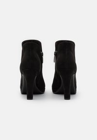 Bottines en suede noir avec une finition lisse, dotées de fermetures éclair sur les côtés et d'un talon aiguille haut. Conçues pour un ajustement serré autour de la cheville.