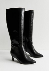 Czarne botki do kolan z błyszczącej skóry, z wydłużonym noskiem i smukłym obcasem. Projekt jest elegancki i minimalistyczny.