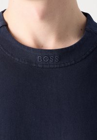 Mörkblå bomullst-shirt med ribbat mönster och korta ärmar. Har en broderad "BOSS"-logotyp på rundhalsen.