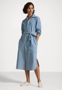 Rochie camasa din denim de culoare albastra deschisa, cu maneci lungi, guler, design cu nasturi in fata, talie legata, slits laterale si doua buzunare. Material din bumbac.