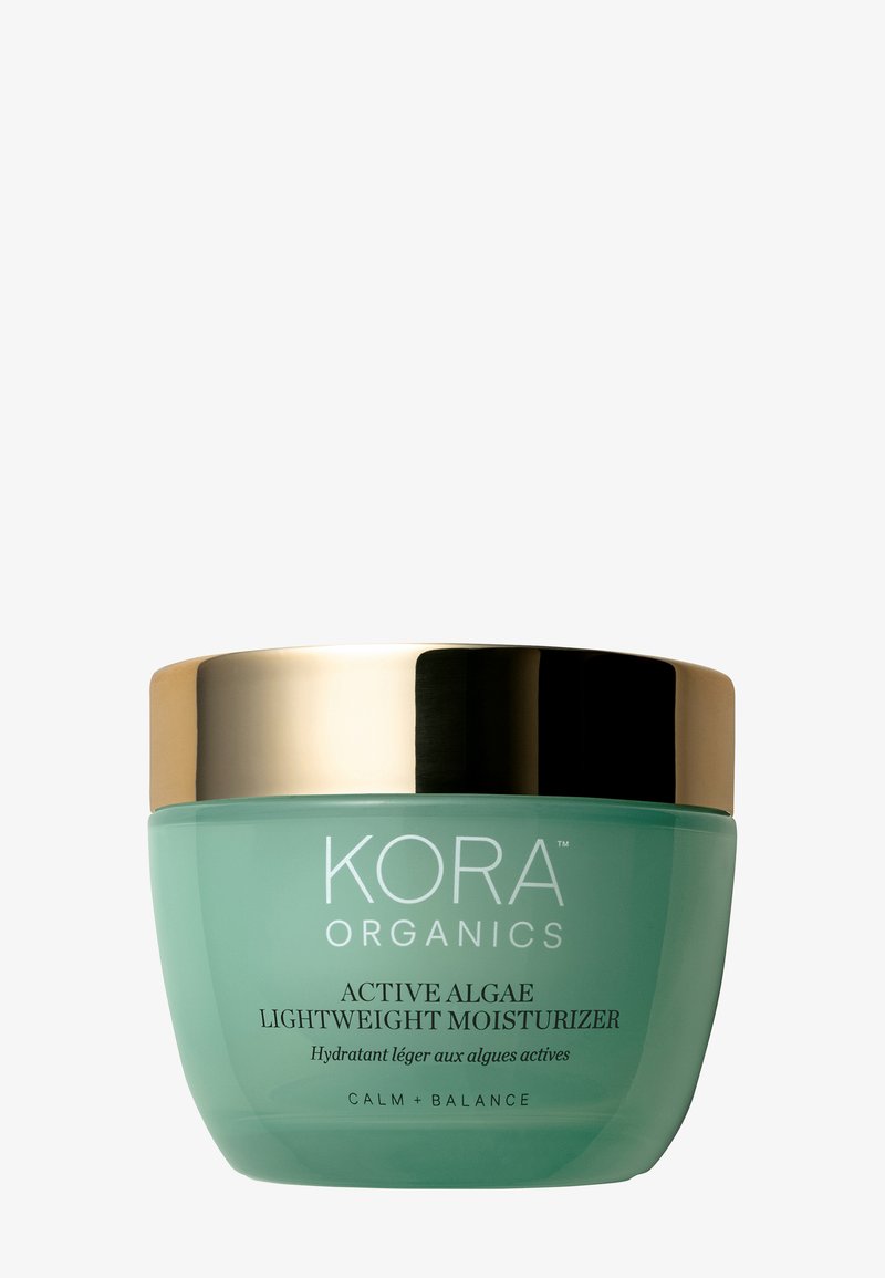 Bocal en verre vert avec un couvercle doré, étiqueté "KORA ORGANICS ACTIVE ALGAE LIGHTWEIGHT MOISTURIZER", texture lisse et forme arrondie.