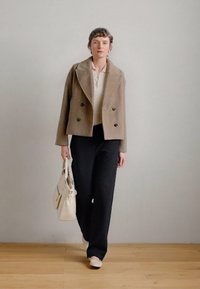 Brūna dubultā jaciņa, krema garām piedurknēm krekls, melni teksturēti platleņķa bikses un krema toņa rokassoma. Līdzeni bēši apavi.