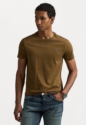 Brown, short-sleeve t-shirt made of smooth fabric, featuring a small logo on the chest. Paired with blue jeans and a silver watch.