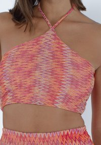 Top corto a halter color rosa brillante e arancione con motivo a zigzag e tessuto testurizzato. Si allaccia al collo con un design aderente.