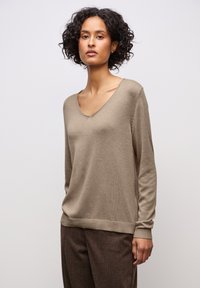 Pull en maille brun clair avec un col en V, des manches longues et des poignets côtelés, associé à un pantalon texturé brun. Texture lisse et coupe décontractée.