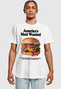 Hvid T-shirt med et farverigt grafisk design af en burger med sesamfrøbolle, salat, tomat, løg og dryppende sauce, plus tekst ovenfor og nedenfor.