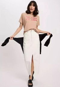 Beżowy t-shirt graficzny z krótkim rękawem, spódnica z wysokim stanem w kolorze białym z rozcięciem z przodu oraz czarne sandały na platformie.