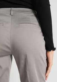 Šedé kalhoty na míru s dvěma zadními kapsami a hladkým povrchem, doplněné černým žebrovaným topem s dlouhým rukávem.