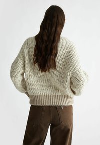 Maglione lavorato a maglia spesso in bianco sporco con orlo a coste, caratterizzato da un motivo testurizzato e una vestibilità comoda. Abbinato a pantaloni marrone scuro.