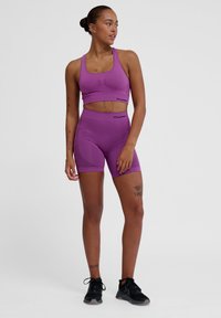 Ensemble de sport violet comprenant un top court en texture côtelée et un short taille haute, tous deux ornés de logo, associés à des baskets noires.