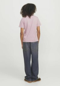 Una camicia rosa chiaro a maniche corte con una vestibilità rilassata, abbinata a jeans in denim blu larghi con tasche posteriori e una vestibilità dritta.