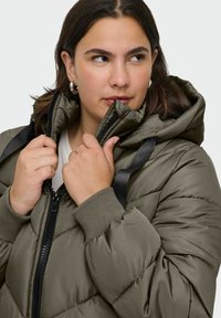 Green puffer jacket with a hood, featuring zipper closure, ribbed cuffs, and black accent straps. The fabric has a smooth, shiny texture.