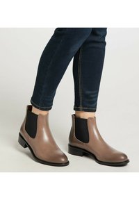 Brune læder Chelsea-støvler med sorte elastiske sidepaneler og en lav hæl. Båret med mørkeblå denim, der har kontrastsyninger.