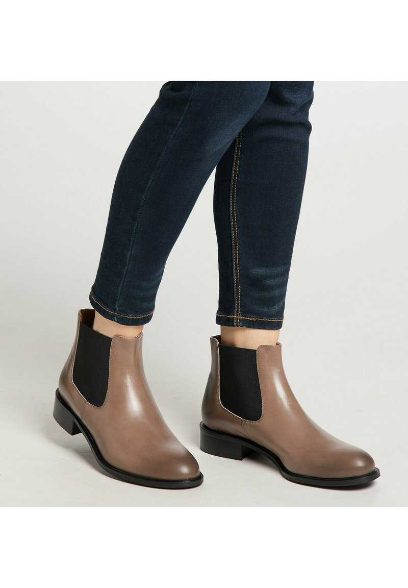 Brune læder Chelsea-støvler med sorte elastiske sidepaneler og en lav hæl. Båret med mørkeblå denim, der har kontrastsyninger.