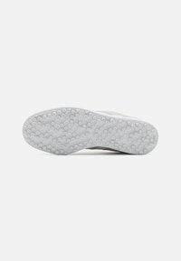 Talpa unei pantof sport, realizată dintr-un material cauciucat alb texturat, cu modele hexagonale pentru aderență și un design curbat al marginii din spate.