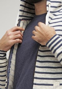 Felpa con zip a righe in crema e blu navy, dotata di cappuccio foderato, cordini piatti e una t-shirt a girocollo blu navy sotto.